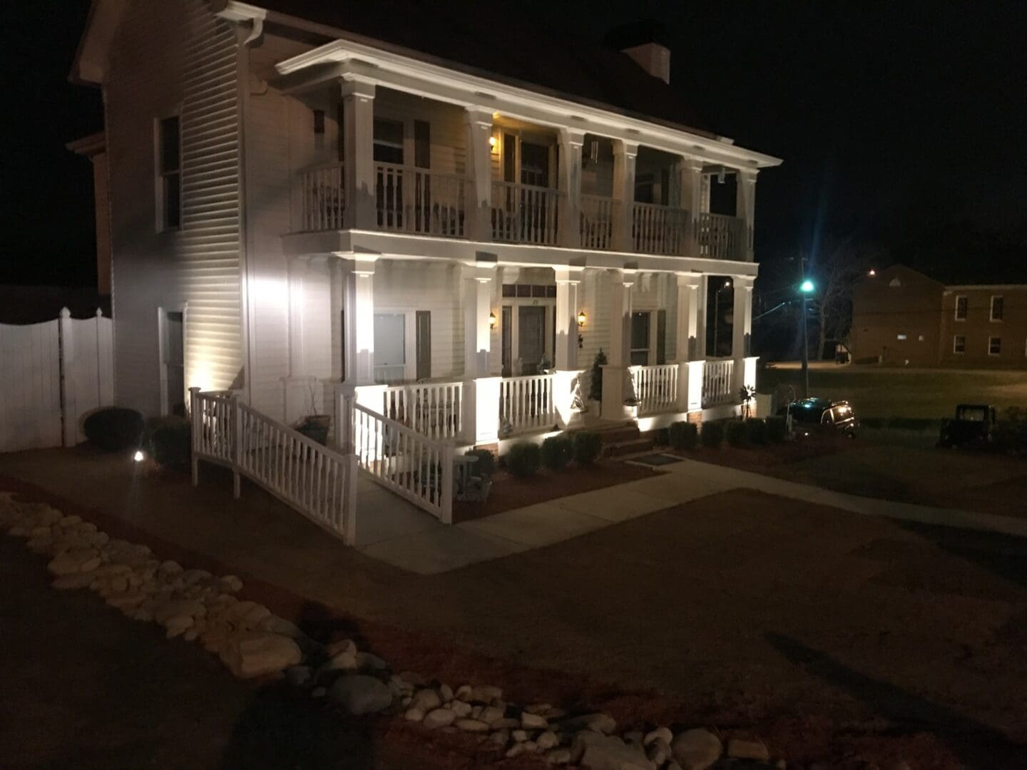 front of a white, 2-story home, at night that is beautifully lit