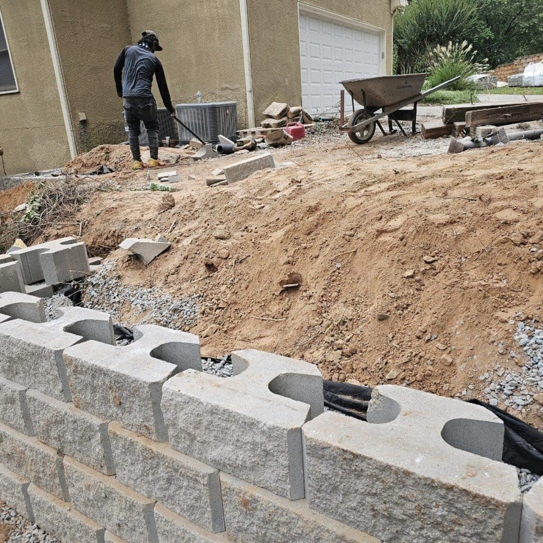 Worker building a concrete block retaining wall outdoors.